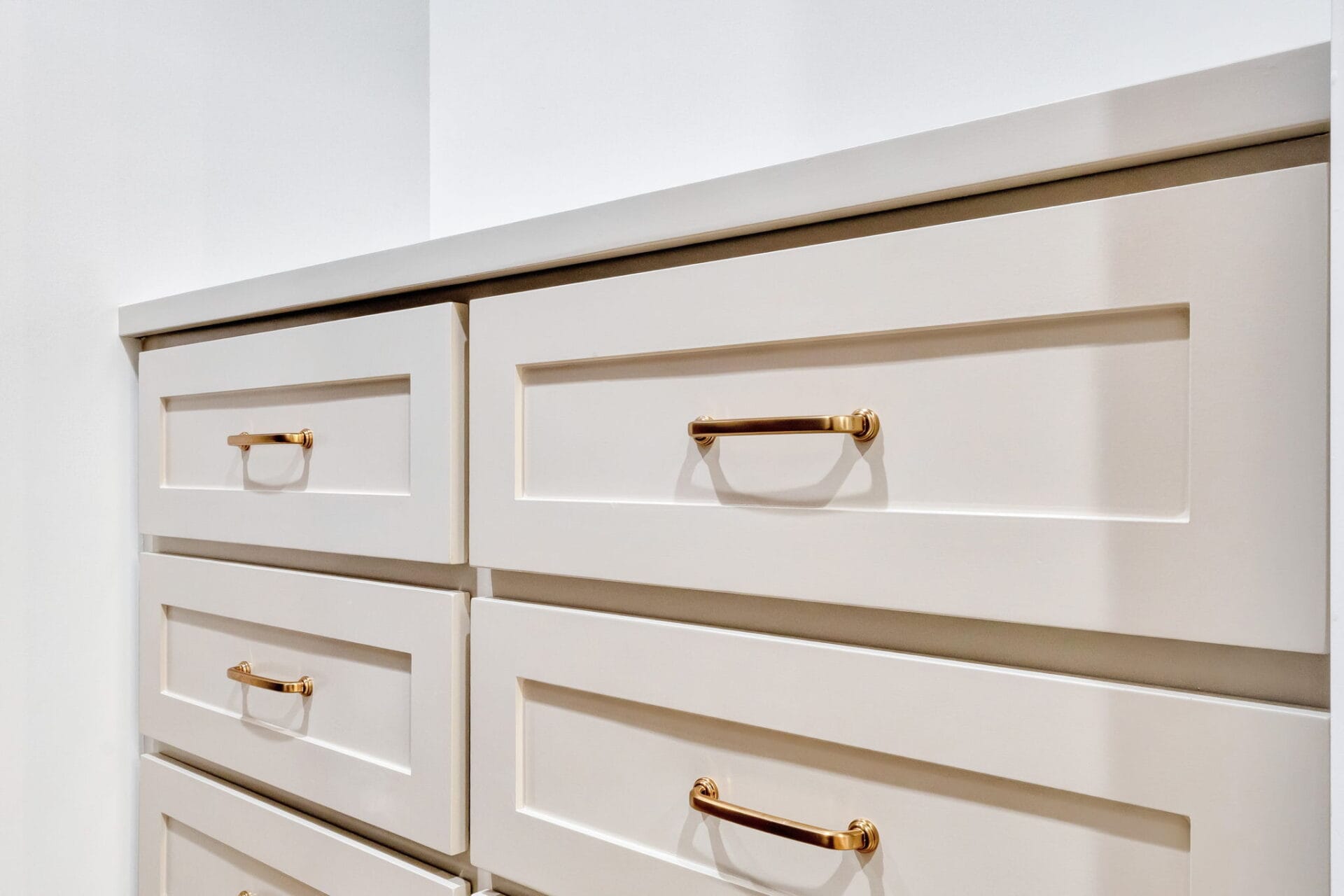A close-up view of beige drawers with gold handles, arranged in two columns, set against a white wall and countertop.