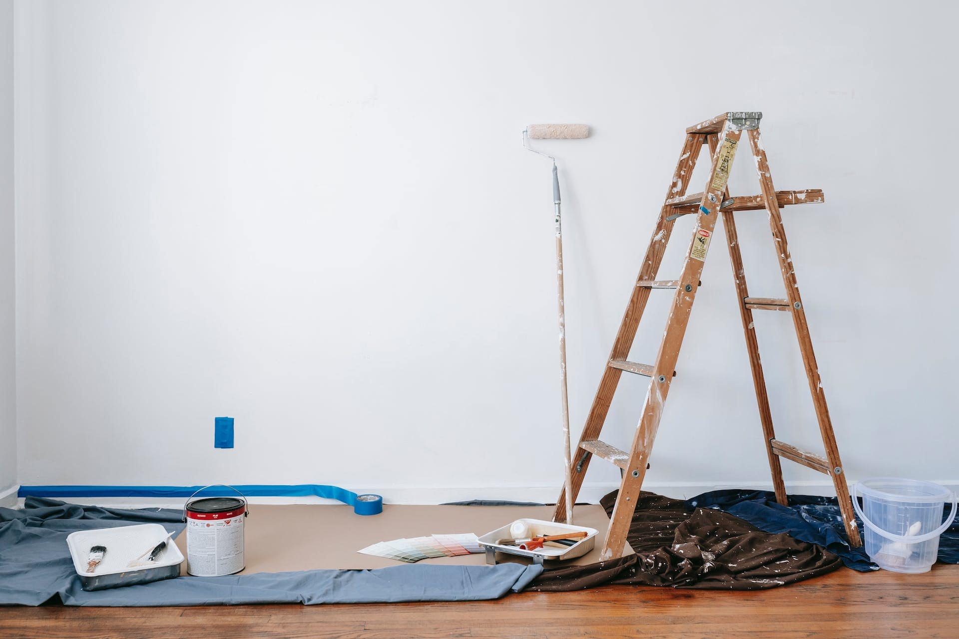 A ladder, paint, and paintbrushes in a room.