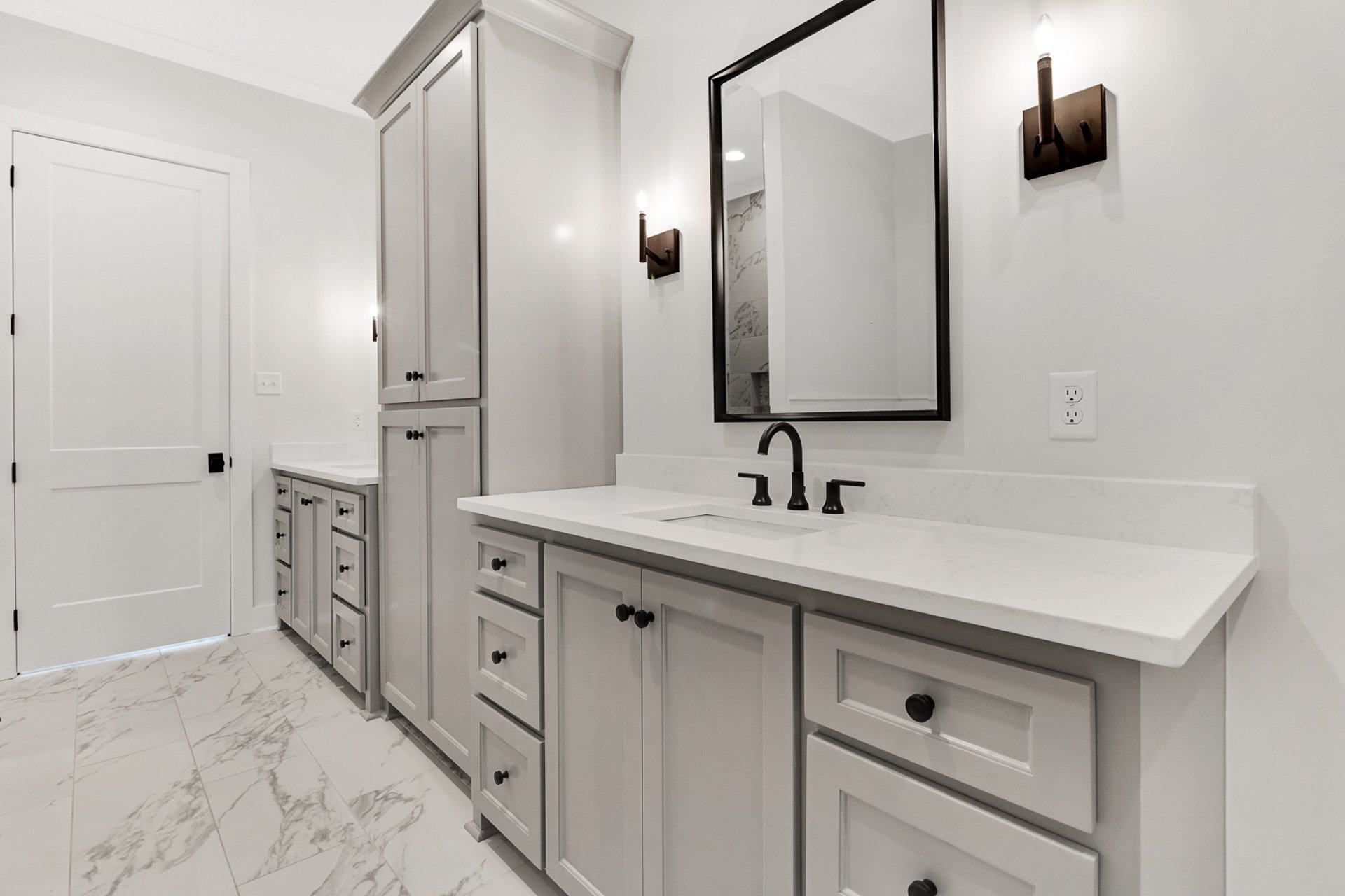A bathroom with white cabinets and marble counter tops.